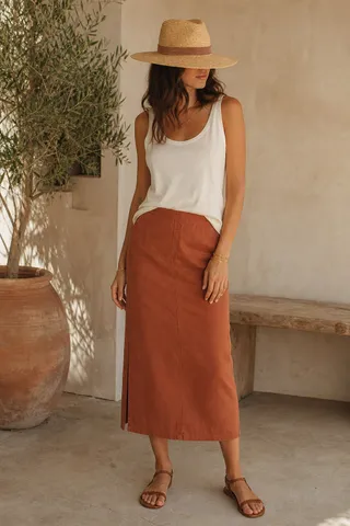A white tank, rust midi skirt and straw hat, styled for a warm day